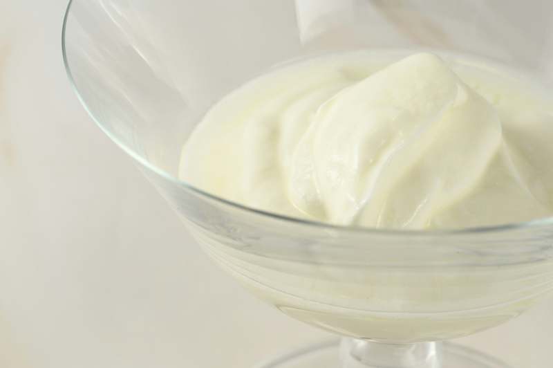 Stainless steel yogurt maker on a clean kitchen counter with jars of creamy homemade yogurt and a glass measuring cup